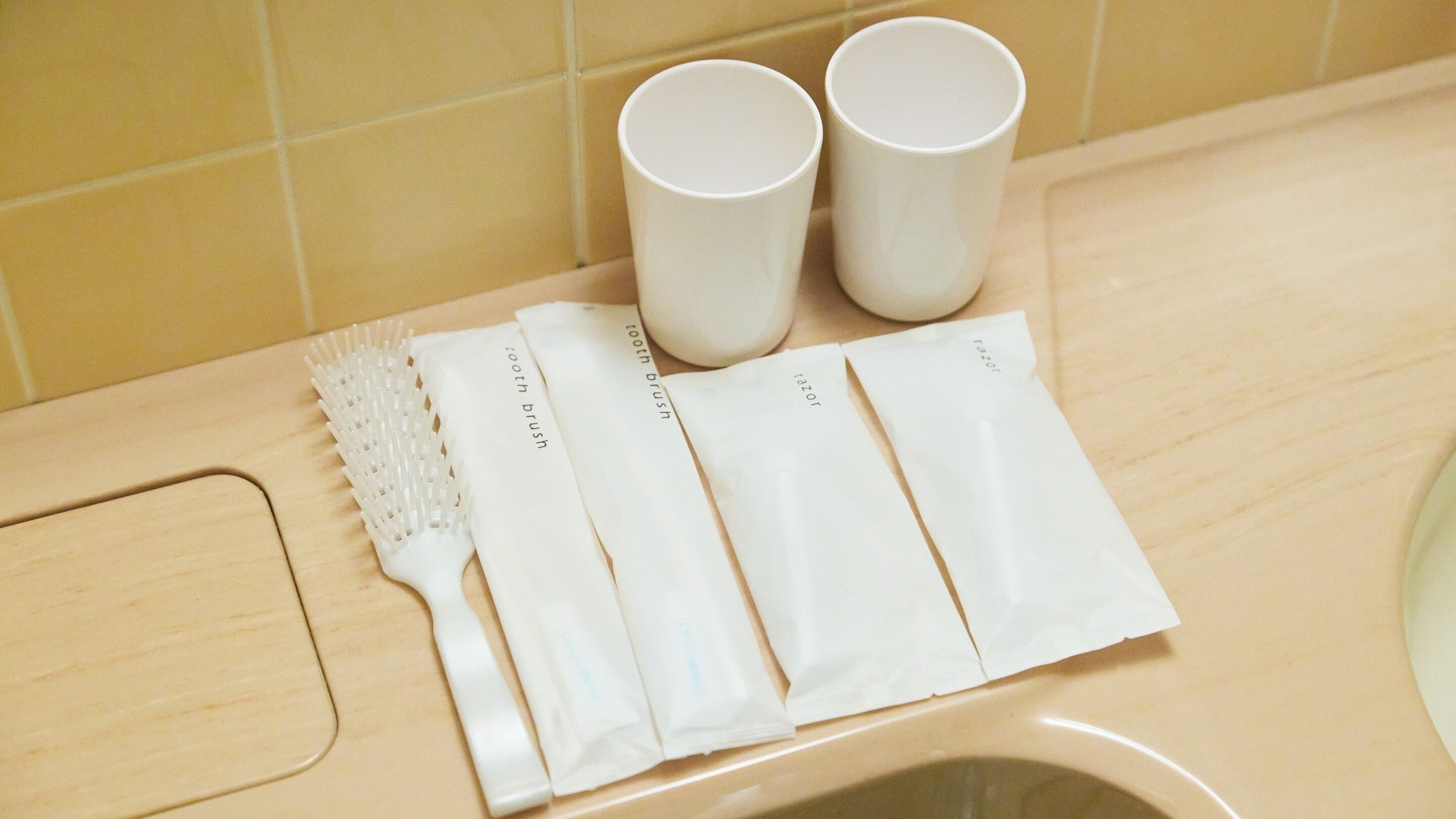 A bathroom sink with a toothbrush, razor, and two cups on the countertop.