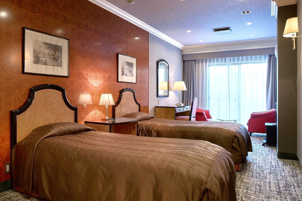 A hotel room with two beds, a desk, a chair, a mirror, and a window with curtains.