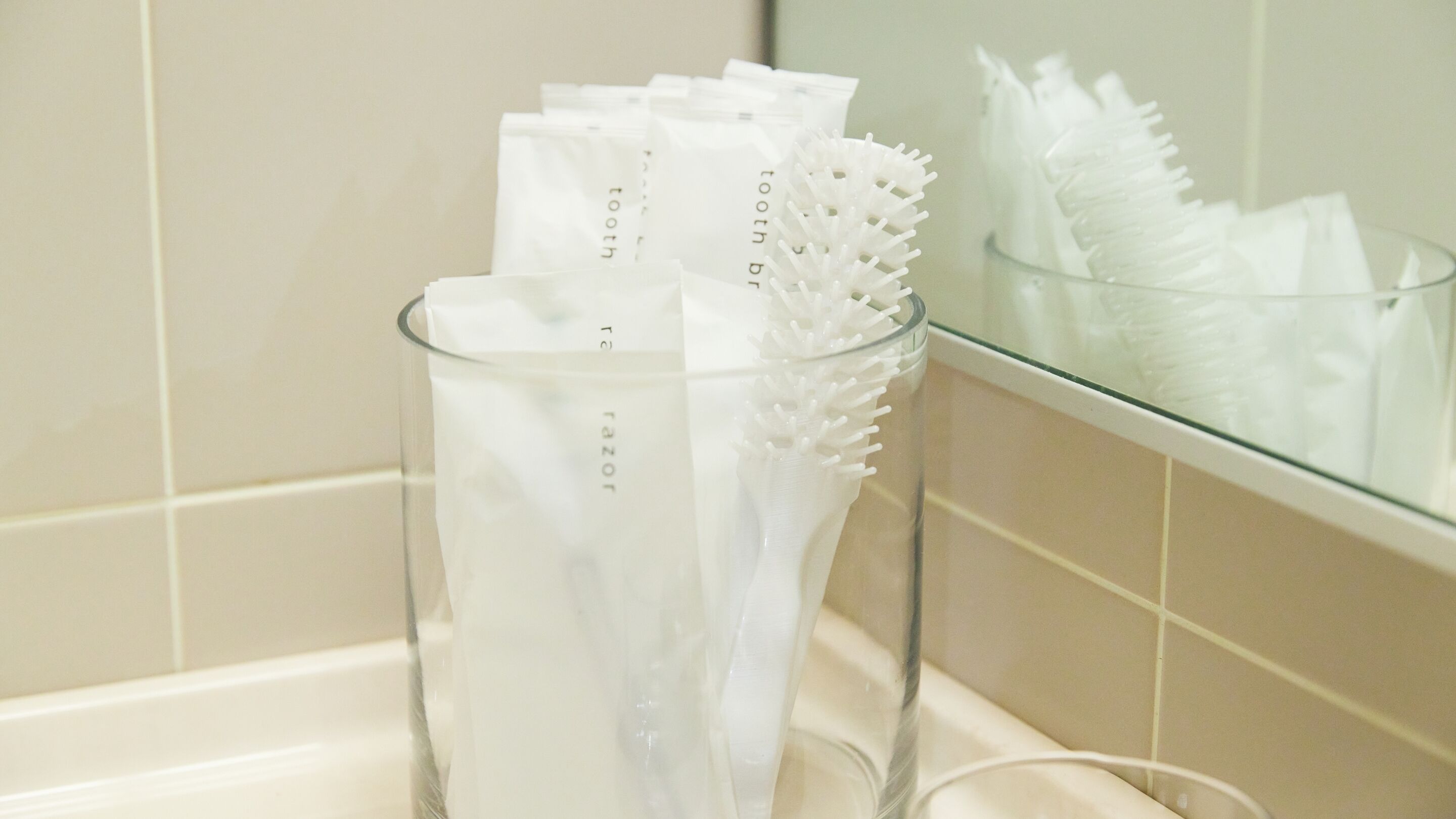A bathroom with a glass container holding toothbrushes and a toothbrush holder with spiky handles.