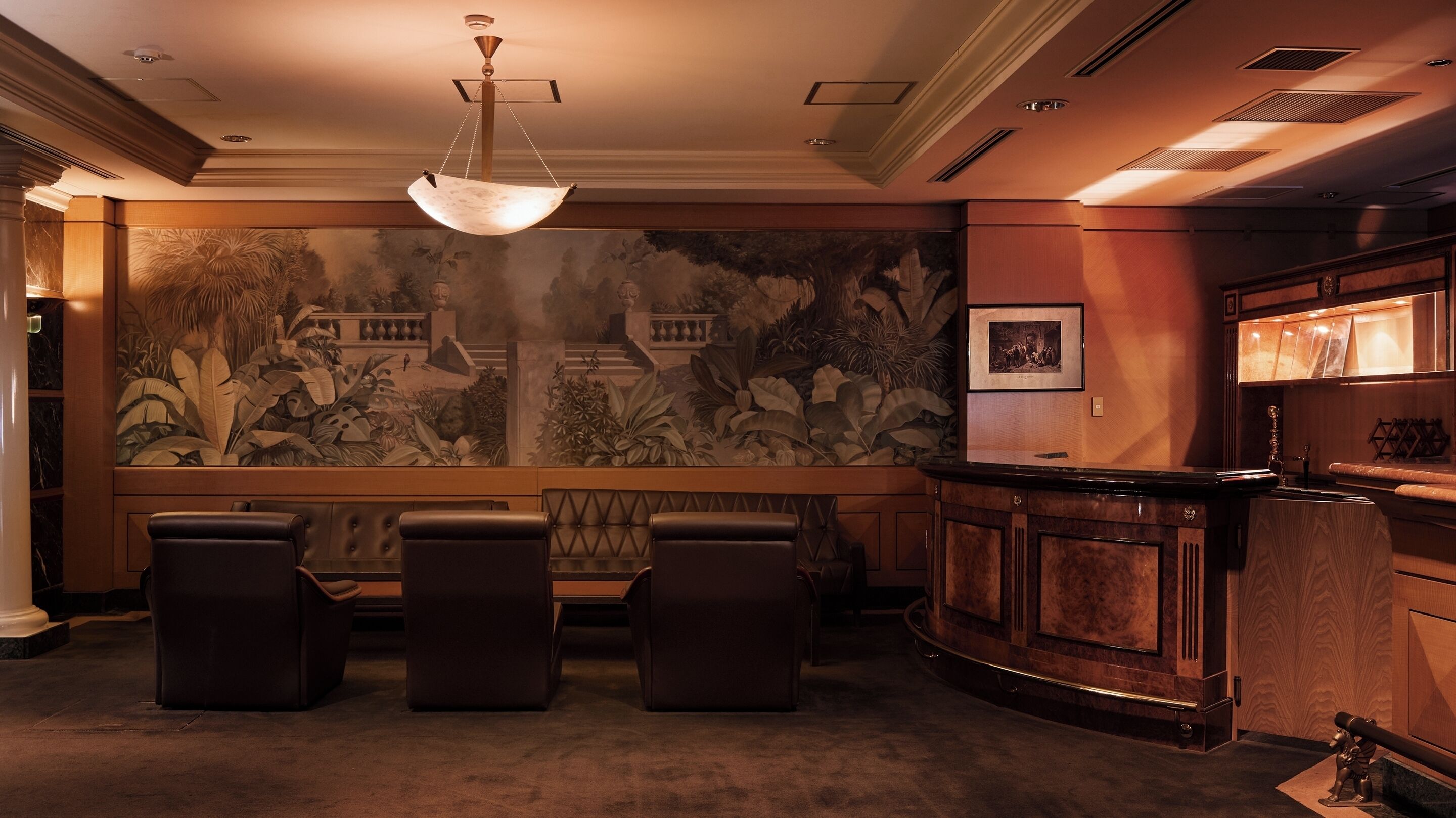 A lobby with a reception desk, a seating area with three chairs, and a large mural on the wall.