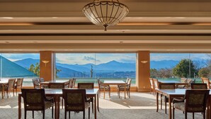 A dining area with tables and chairs, large windows with a mountain view, and a decorative ceiling light. - Mission Hills Hotel (Minano)