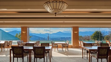 Un comedor con mesas y sillas, ventanas amplias con vistas a la montaña y una lámpara decorativa en el techo.