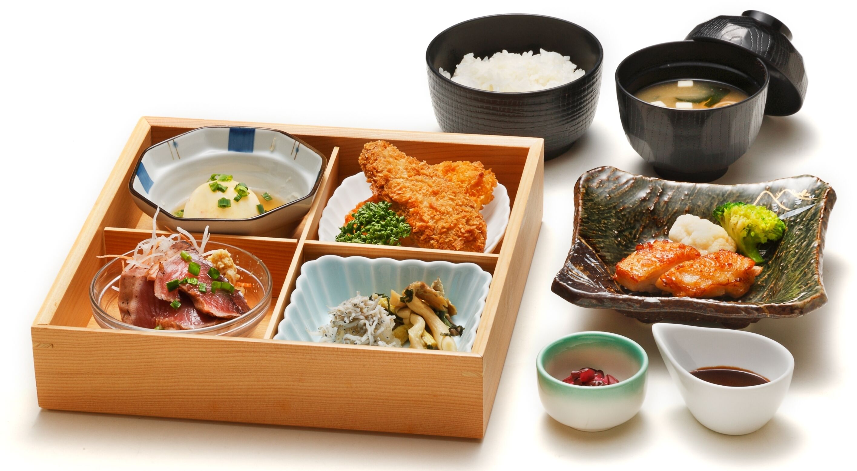 A traditional Japanese bento box with various food items including rice, fish, and vegetables.