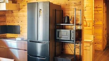 A compact kitchen with a stainless steel refrigerator, a microwave, and a kettle on a shelf.