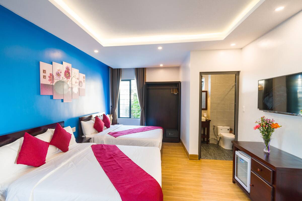 A hotel room with two beds, a TV, a small fridge, and a bathroom visible through an open door.