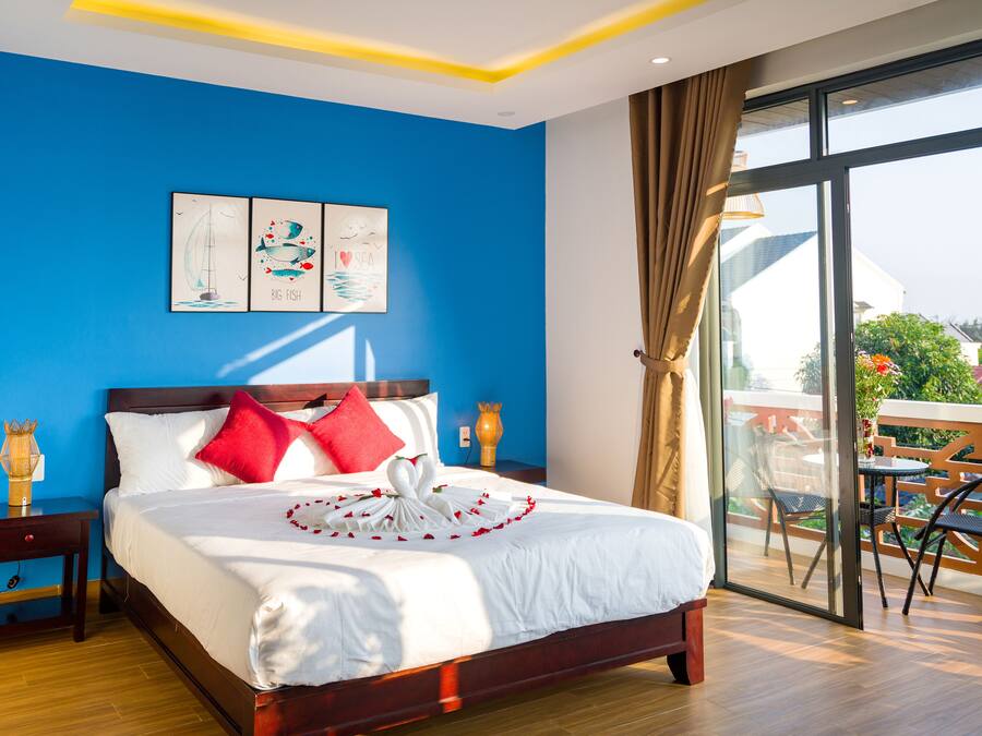 A hotel room with a large bed, a balcony with outdoor furniture, and artwork on the wall.