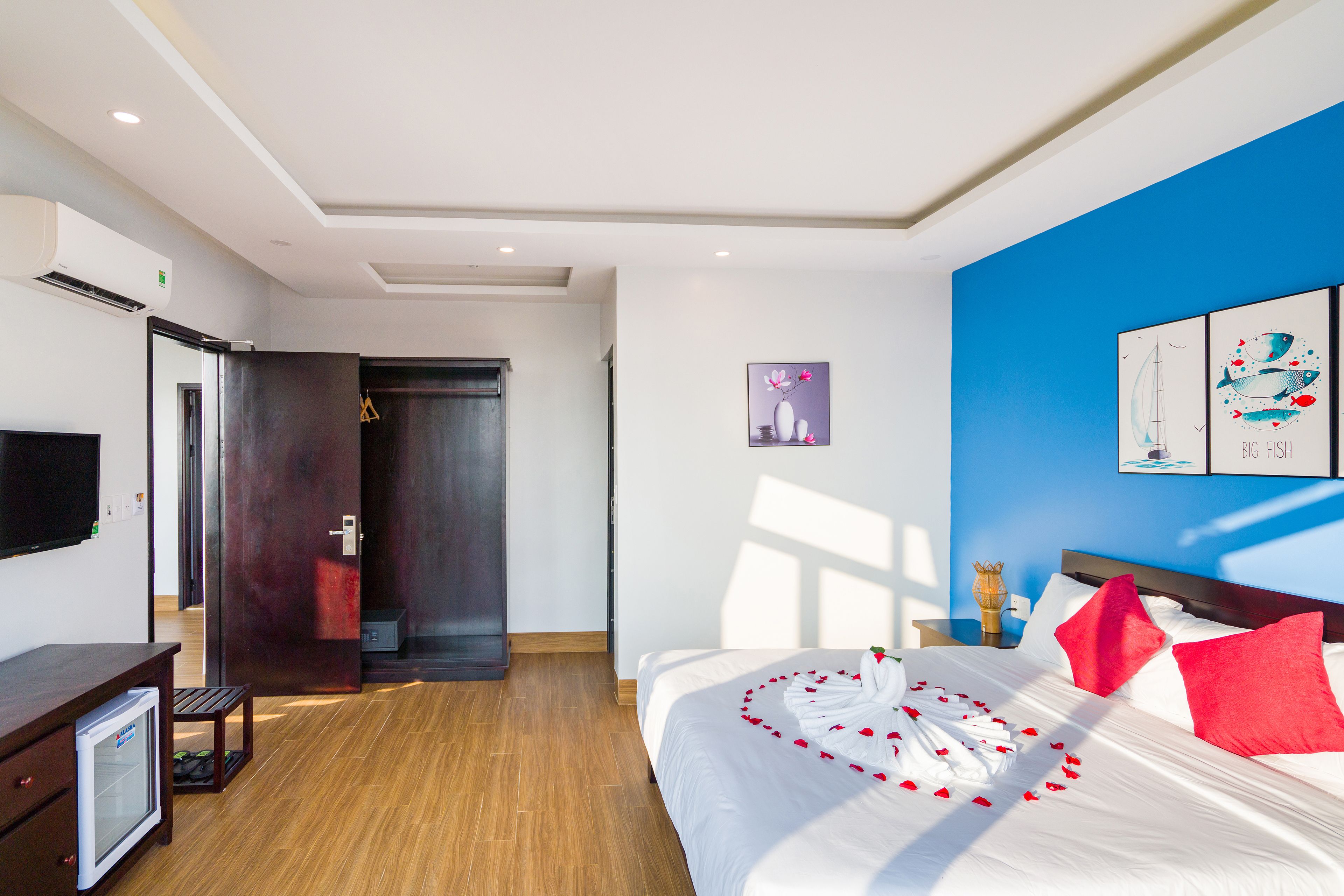 Een hotelkamer met een bed, een bureau, een kleine koelkast en kunstwerken aan de muren.