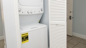 Ein Waschraum mit einer Waschmaschine und einem Trockner mit Frontlader, einer Tür mit Klappläden und einem gefliesten Boden.