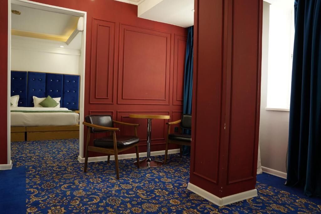 A hotel room with a bed, two chairs, a small table, and a red accent wall.