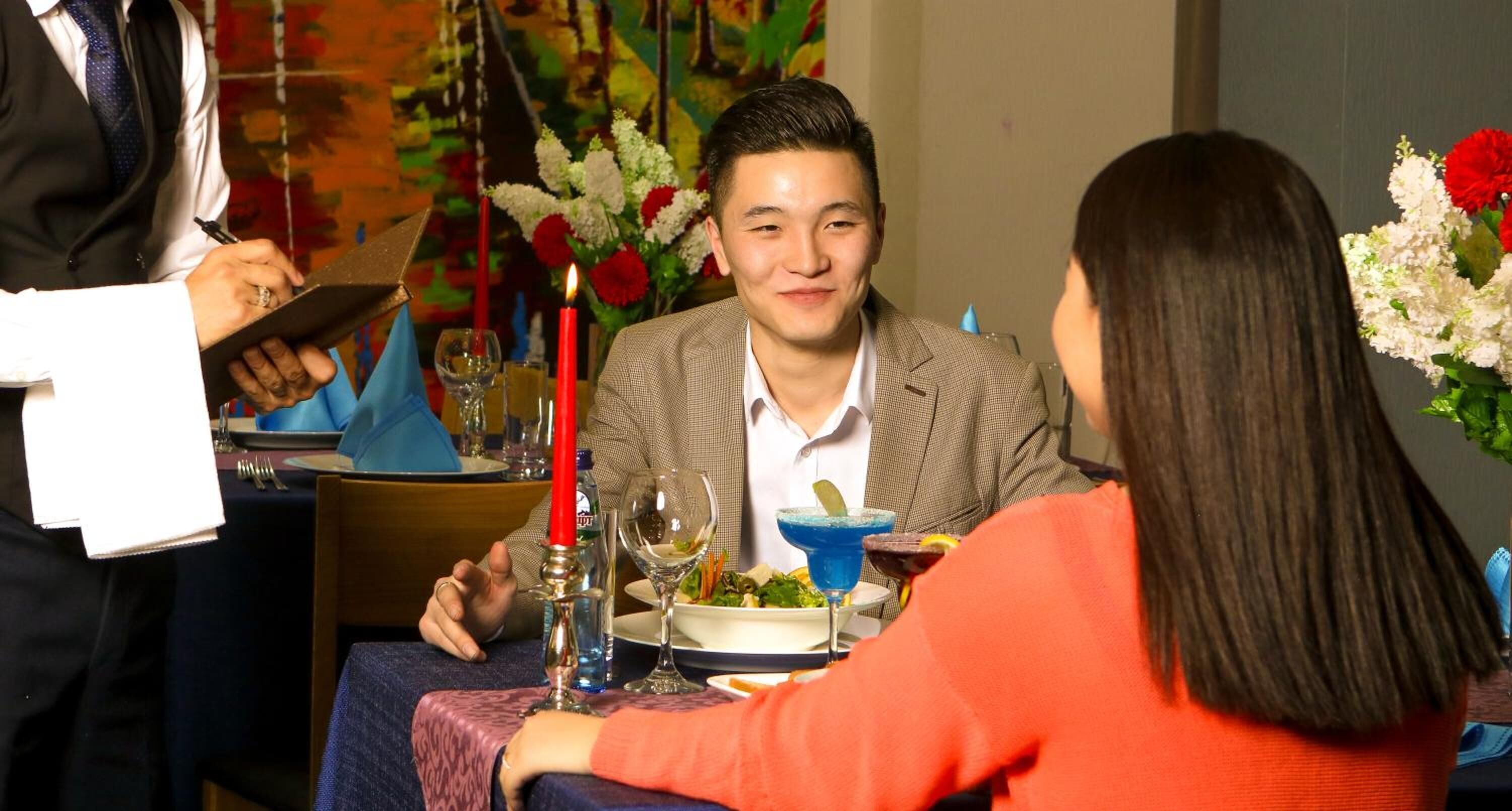 A dining table set with a candle, wine glasses, and a bowl of salad.