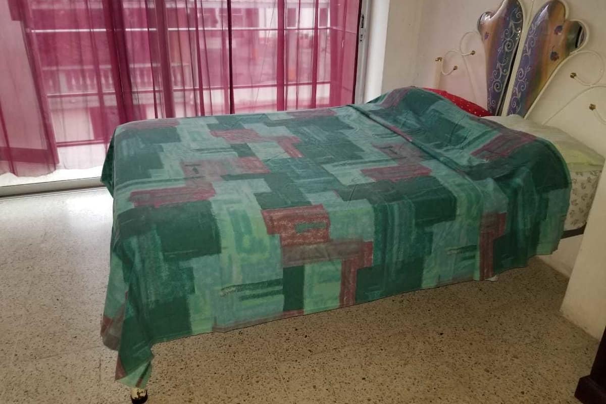 A bed with a patterned bedspread in a room with a window and curtains.
