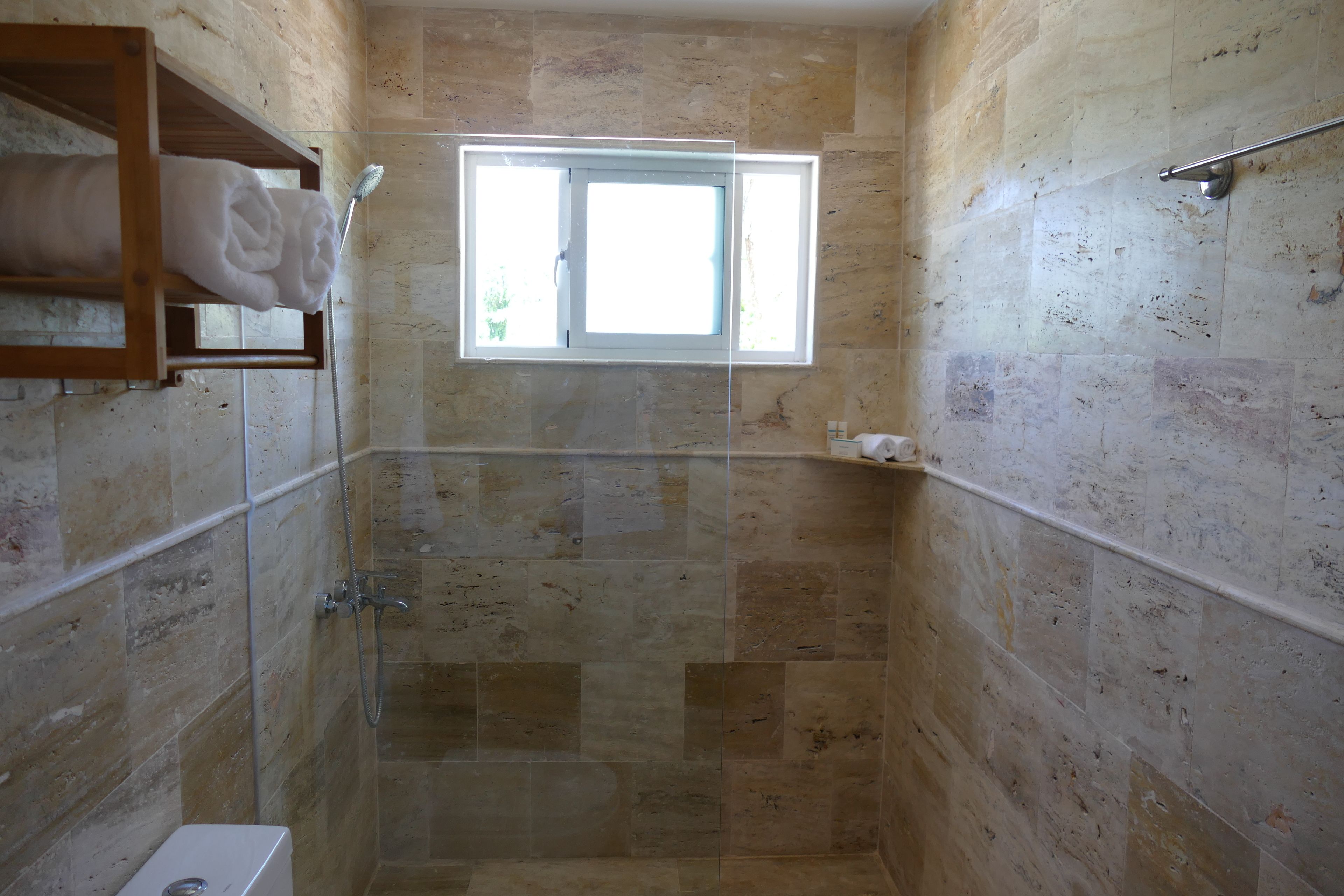 Un pequeño baño con azulejos, una ventana, un perchero y un cabezal de ducha.