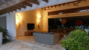 Un espace de vie extérieur comprenant un canapé, un téléviseur et des lampes fixées au mur.