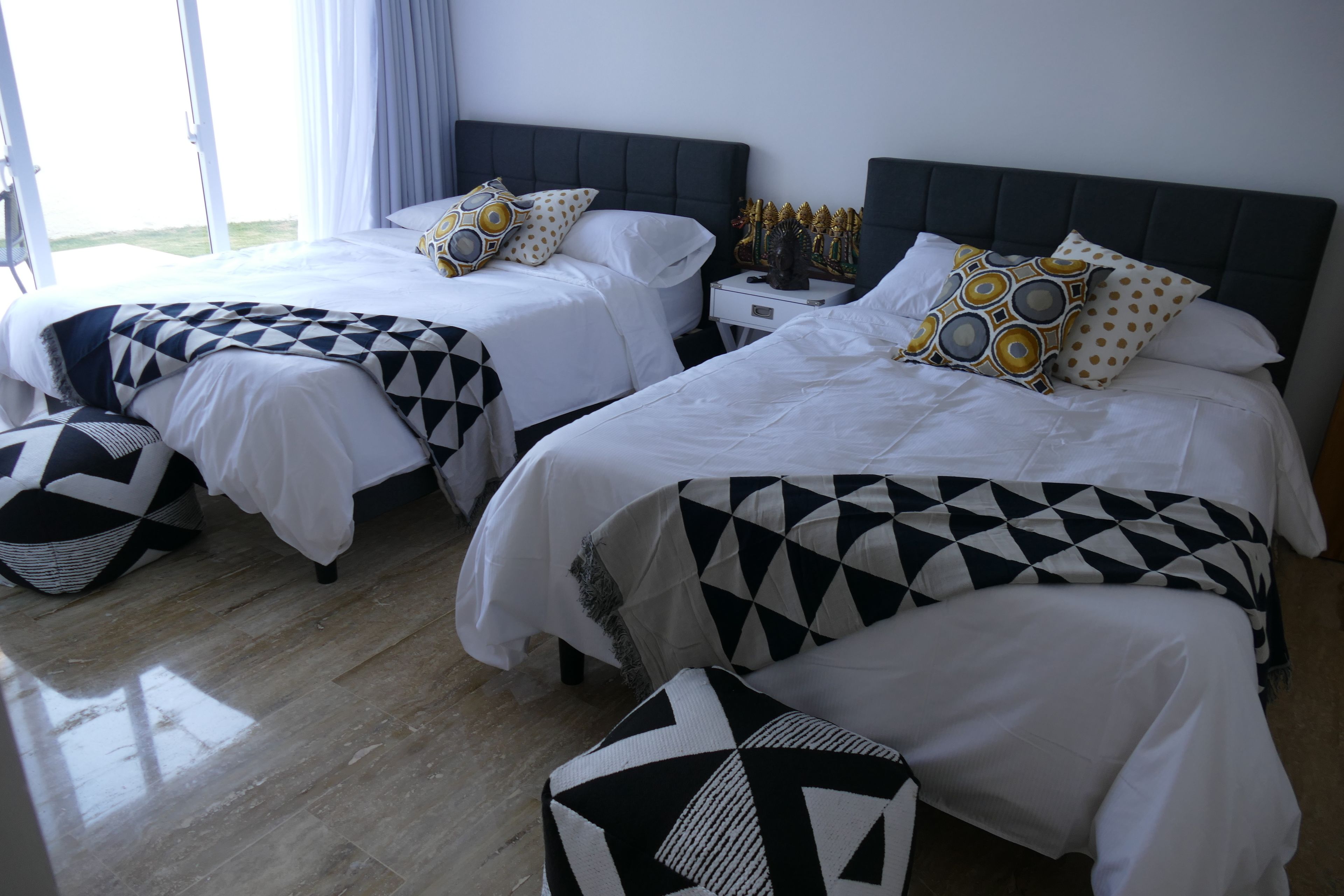 Une chambre d’hôtel avec deux lits, chacun recouvert d’une couvre-lit à motifs géométriques et agrémenté d’oreillers assortis. Une table de chevet avec des objets décoratifs se trouve entre les deux lits.