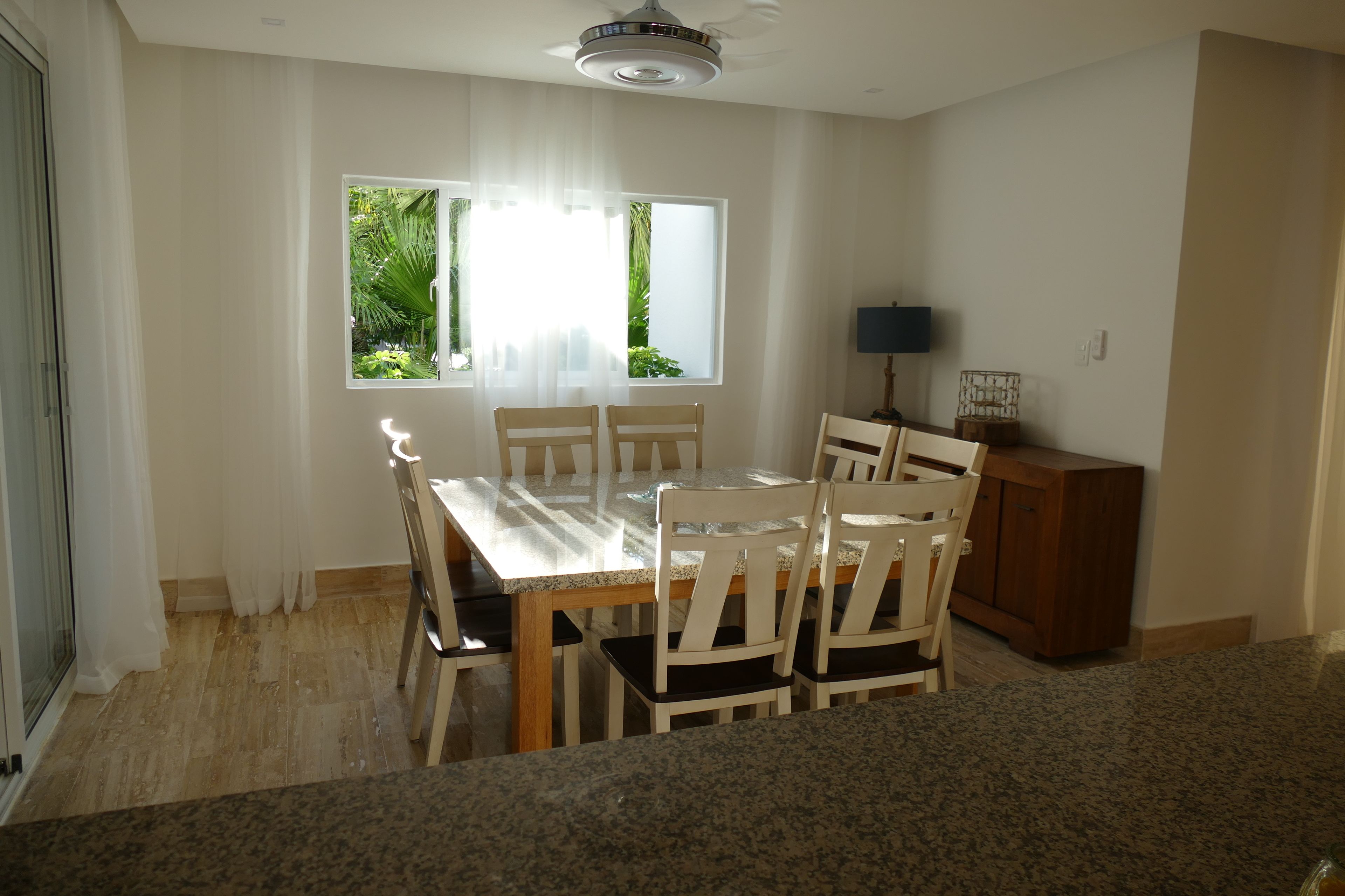 A dining area with a table and chairs, a window with curtains, a ceiling fan, and a cabinet.