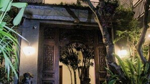 Uma entrada tradicional com degraus que levam a uma porta, cercada por vegetação exuberante e estátuas decorativas.