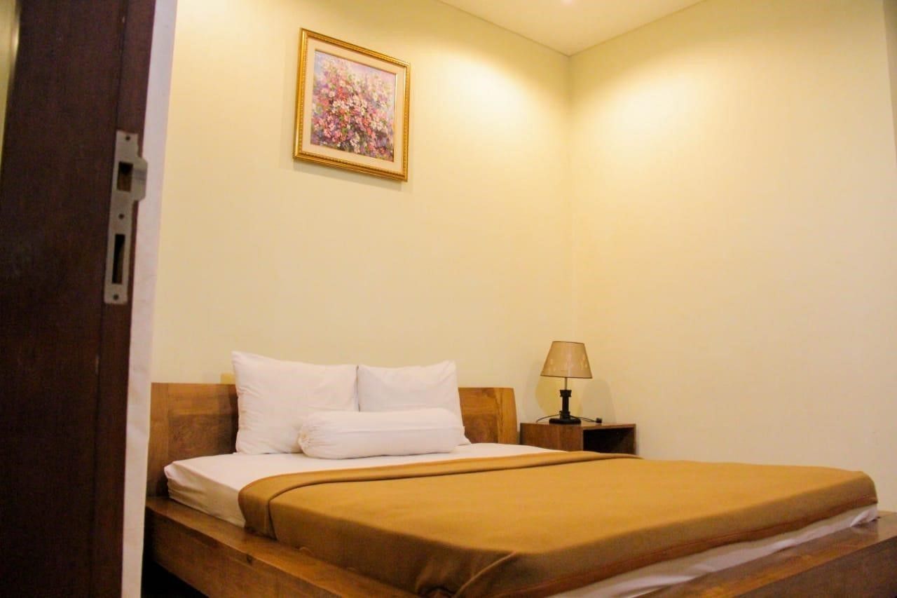 A single bed with white and brown bedding, a nightstand with a lamp, and a framed floral painting on the wall.