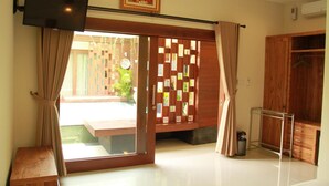 Quarto com porta de vidro deslizante para uma varanda, um armário de madeira e uma televisão fixada na parede.