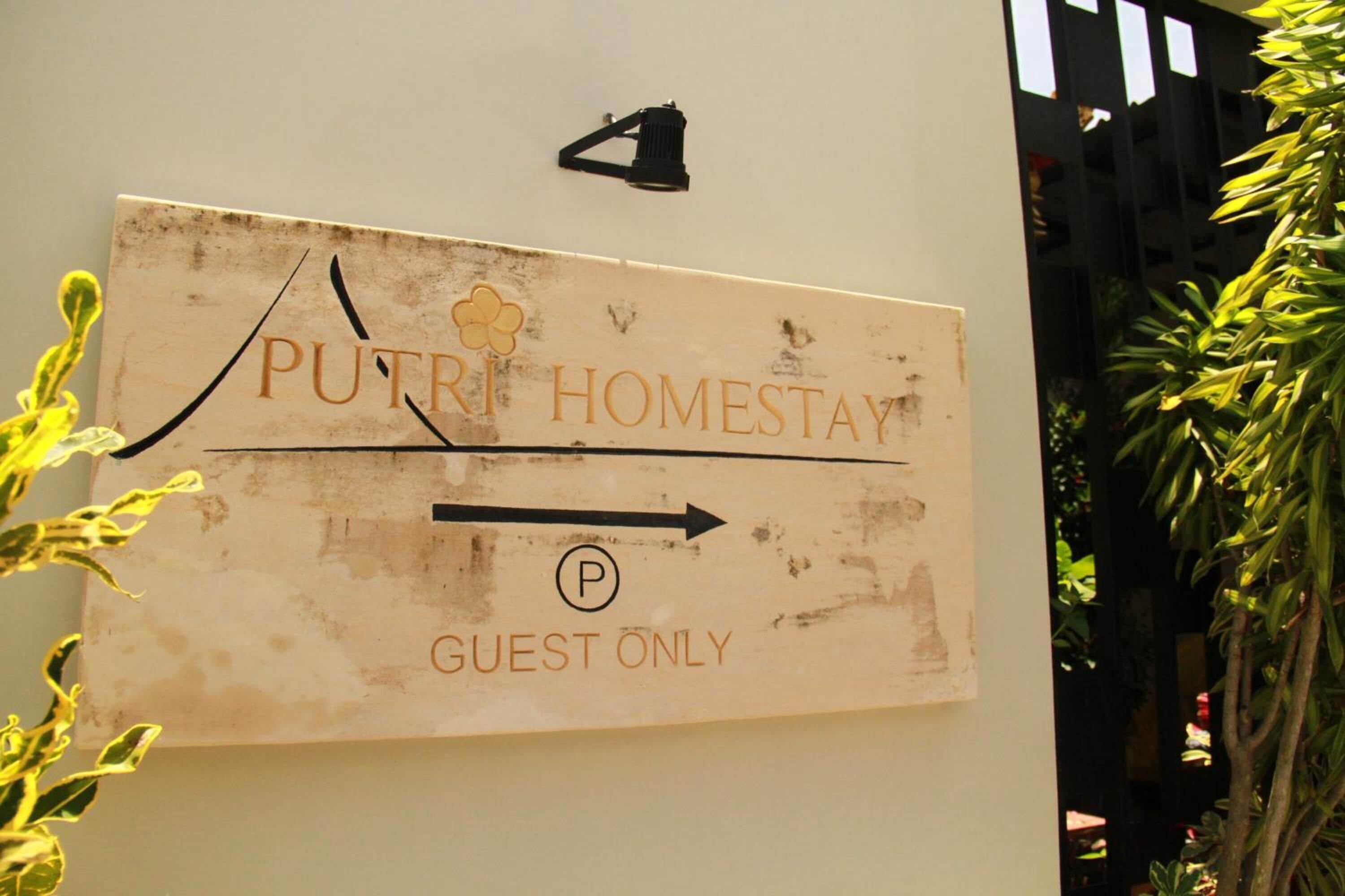 A sign for "PUTRI HOMESTAY" with a guest-only parking symbol and an arrow pointing right.