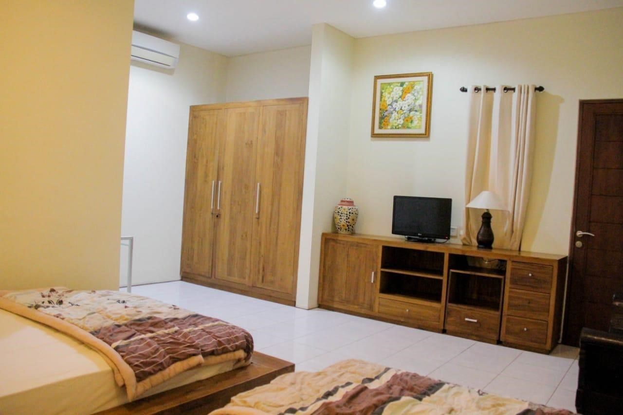 A bedroom with a bed, a wooden wardrobe, a TV on a wooden stand, and a painting on the wall.