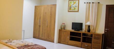 A bedroom with a bed, a wooden wardrobe, a TV on a wooden stand, and a painting on the wall.