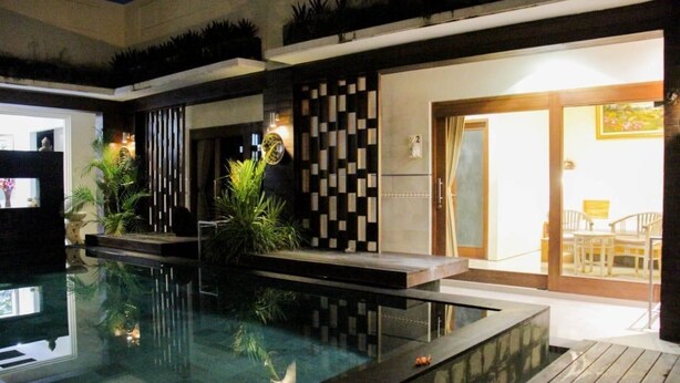 Piscina interna com design moderno, rodeada por plantas e um deck de madeira.