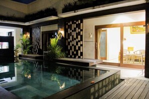 An indoor swimming pool with a modern design, surrounded by plants and a wooden deck.