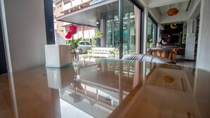 Um hall de hotel moderno com uma mesa de centro de vidro, um vaso branco com uma rosa vermelha, e vista para a rua.