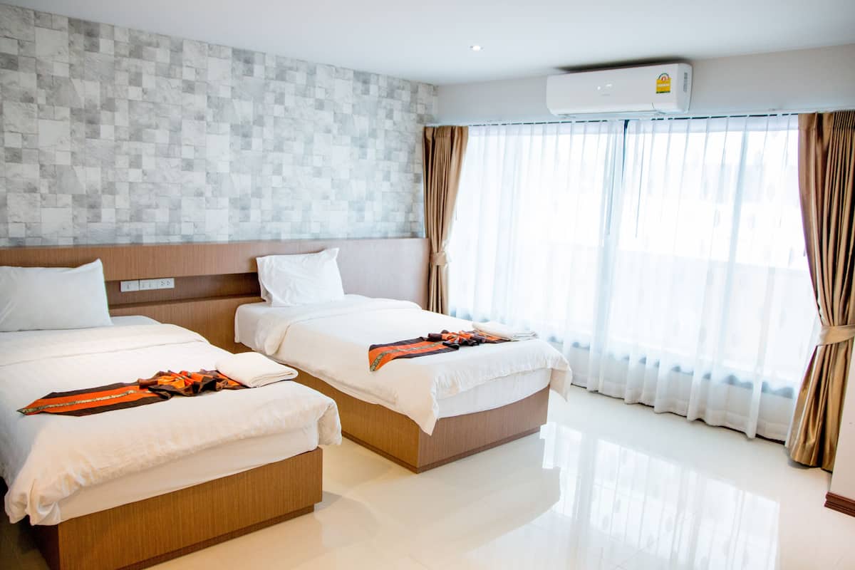 Habitación de hotel con dos camas, pared de azulejos, unidad de aire acondicionado y un amplio ventanal con cortinas.