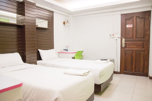 Quarto de hotel com duas camas, uma cabeceira de madeira, uma cadeira verde, uma mesinha e uma porta com um aviso.