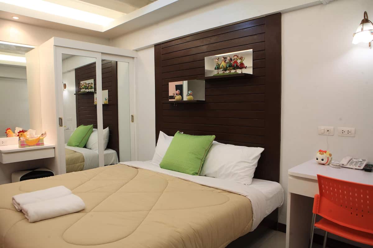 Habitación de hotel con cama, escritorio, silla, espejo y estante de pared con objetos decorativos.