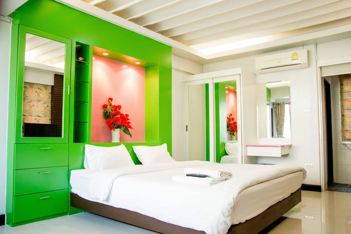 Un dormitorio moderno con una pared de acento verde, una cama grande con ropa de cama blanca, una mesita de noche y un espejo.