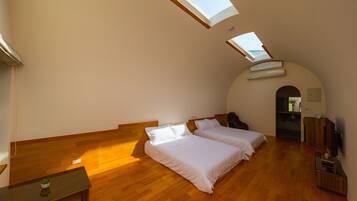 A room with two beds, a small table, a TV, and a skylight.