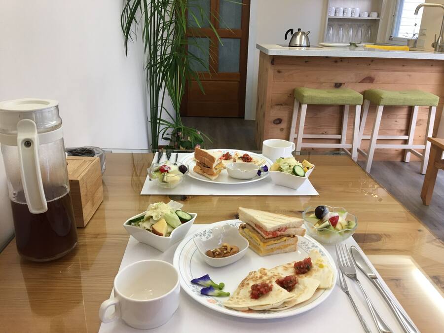 A breakfast table with various dishes, a coffee maker, and a kitchen in the background.