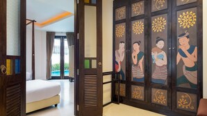 A hotel room with a bed, a large wooden door with traditional artwork, and a view of the outdoors. - Phuket Ratchamaka Pool Villa (Chalong)