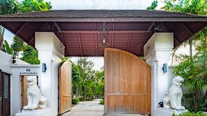 A traditional entrance with a wooden gate, white walls, and two lion statues. - Phuket Ratchamaka Pool Villa (Chalong)