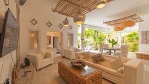 A spacious living area with white sofas, a wicker coffee table, and a TV on the wall. - Smiling Cactus Villa (Seminyak)