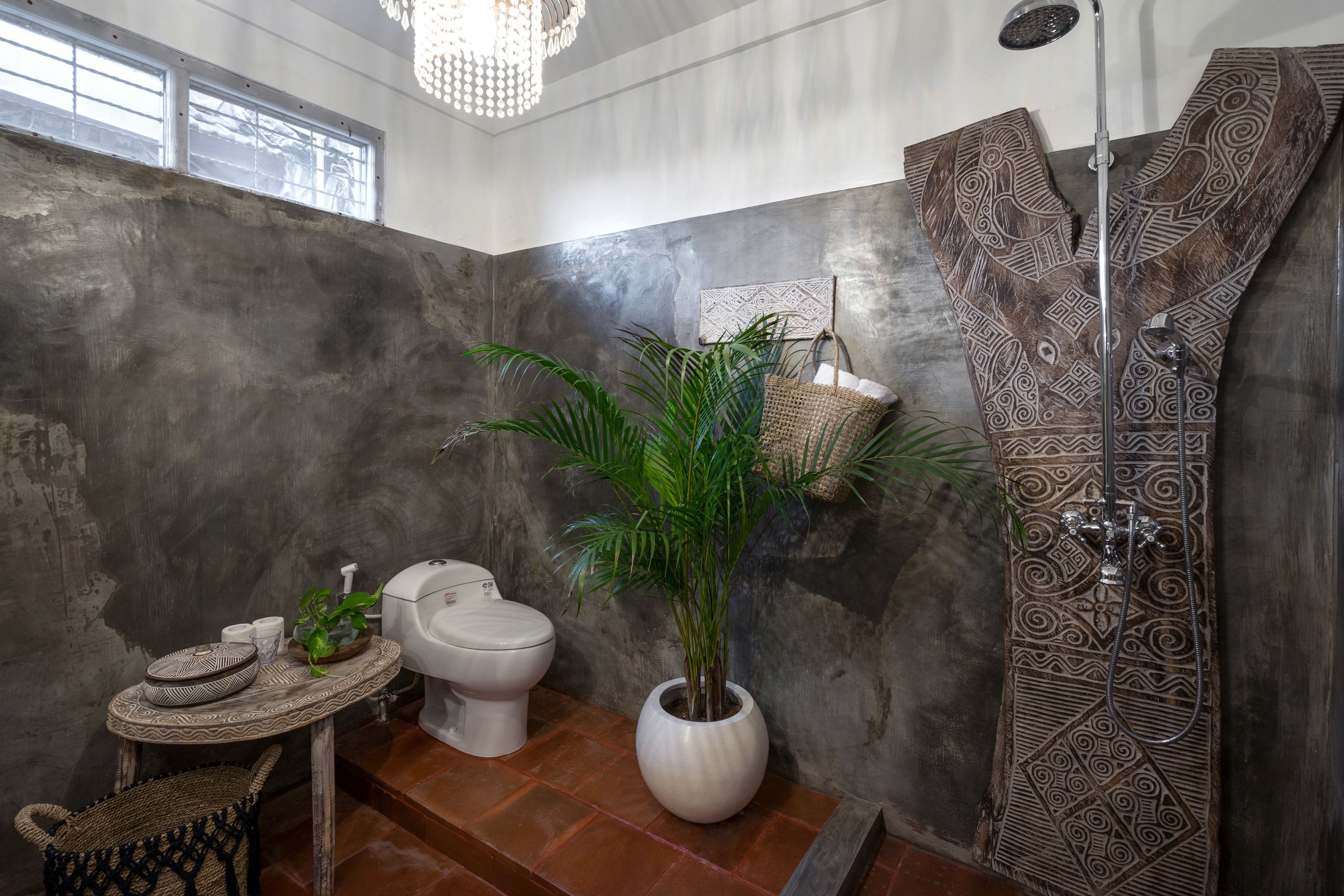 A bathroom with a concrete wall, a shower with a patterned door, a toilet, a sink with decorative bowls, and a potted plant.