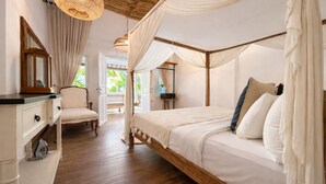 A bedroom with a four-poster bed, a bedside table, a chair, and a hanging light fixture. - Smiling Cactus Villa (Seminyak)