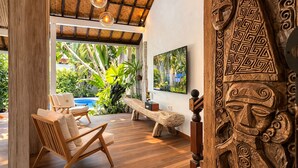 A wooden bench, a wooden chair, and a wooden sculpture in a room with a wooden floor and a thatched ceiling. - Smiling Cactus Villa (Seminyak)