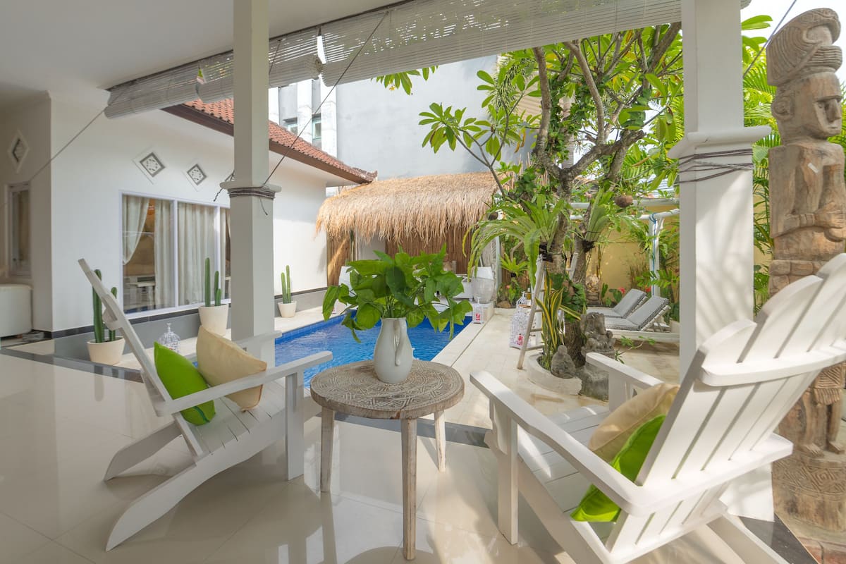 A poolside area with a thatched roof, lounge chairs, and potted plants.