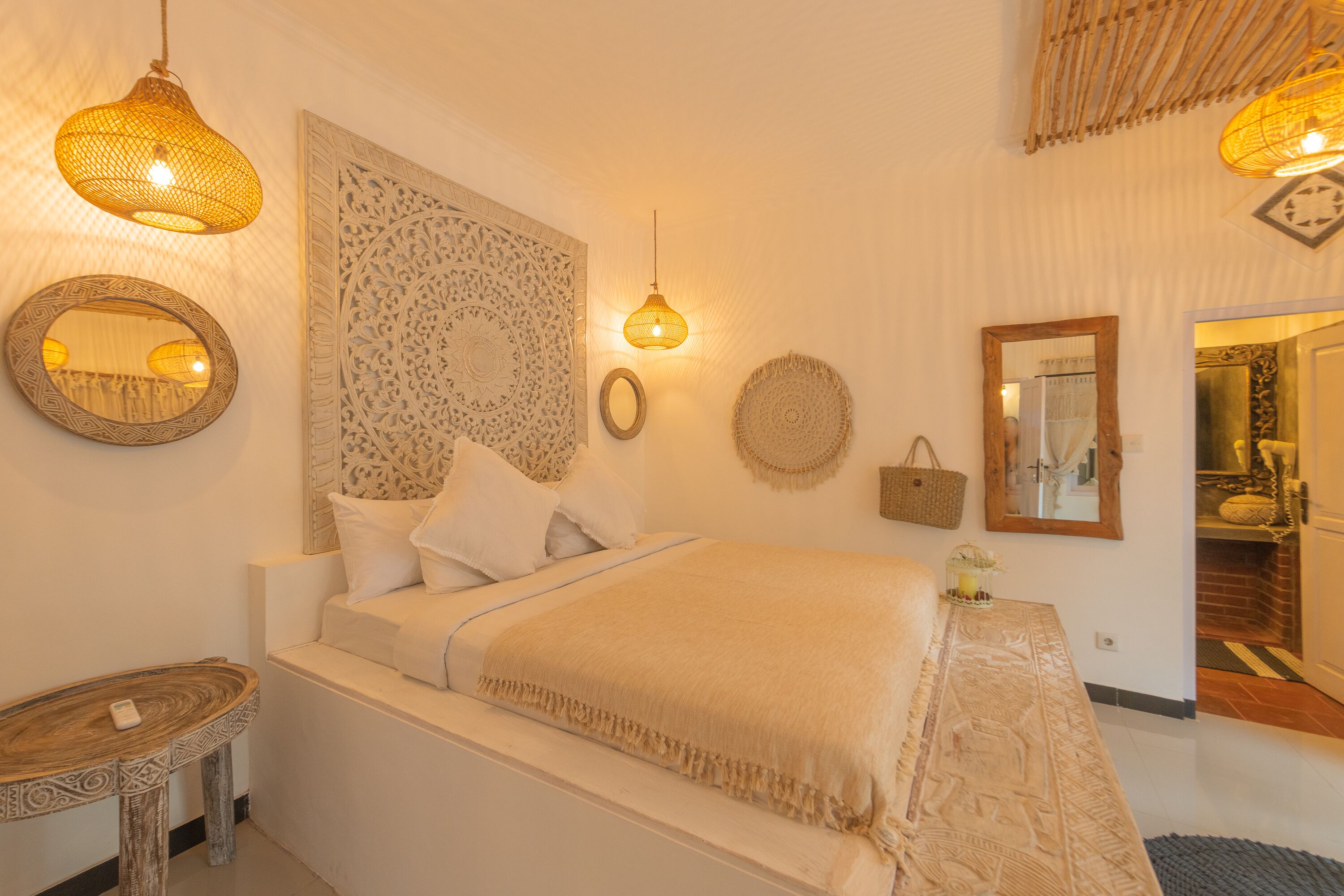 A bedroom with a bed, a bedside table, a wall-mounted mirror, and decorative wall hangings.