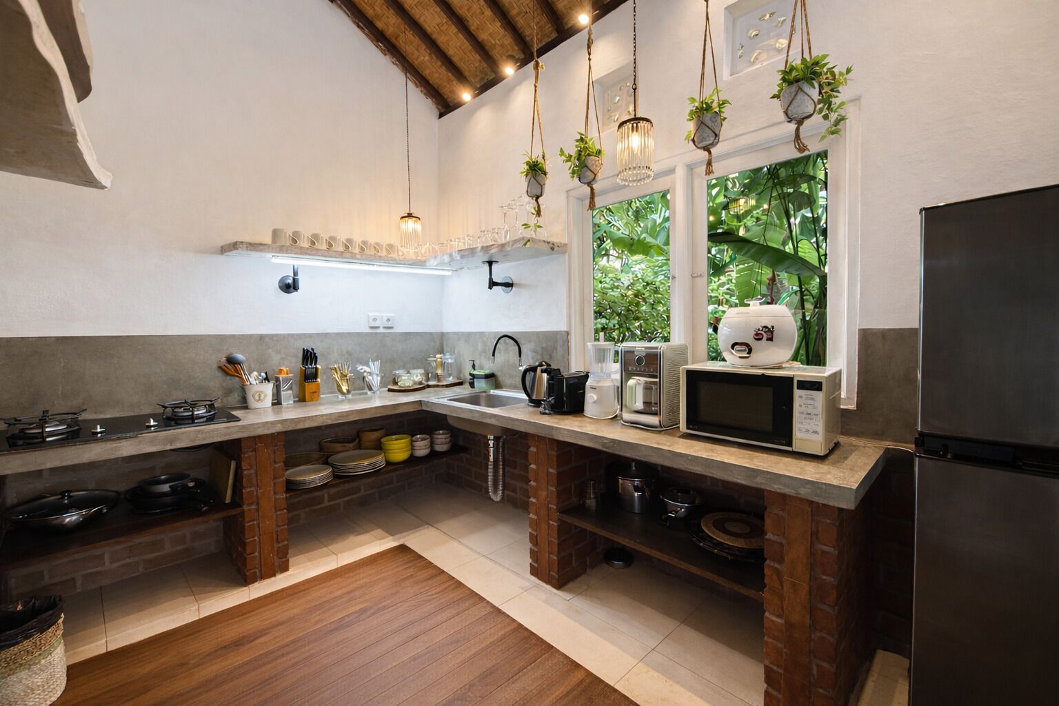 A kitchen with a brick island, stainless steel appliances, hanging plants, and a window with a view of greenery.