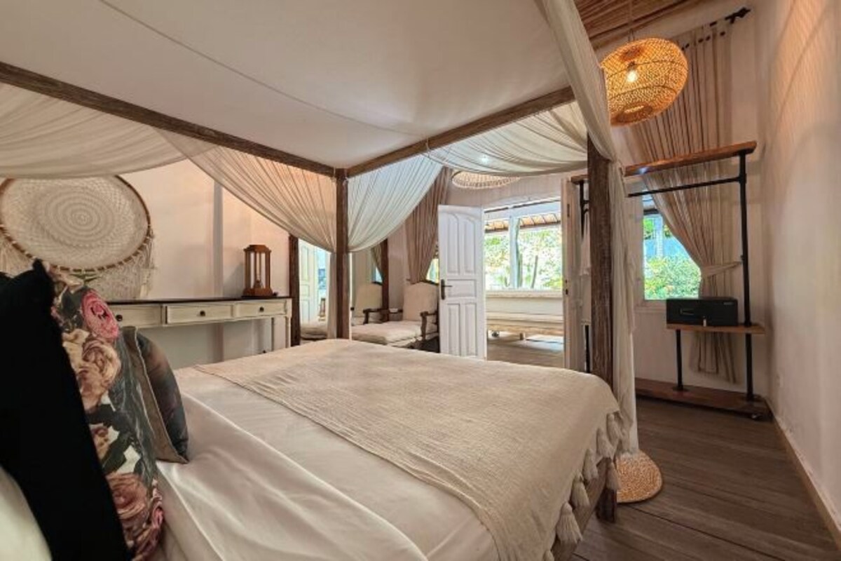 Um quarto espaçoso com uma cama grande, uma mesa de cabeceira, uma cadeira e uma janela com vista para vegetação.