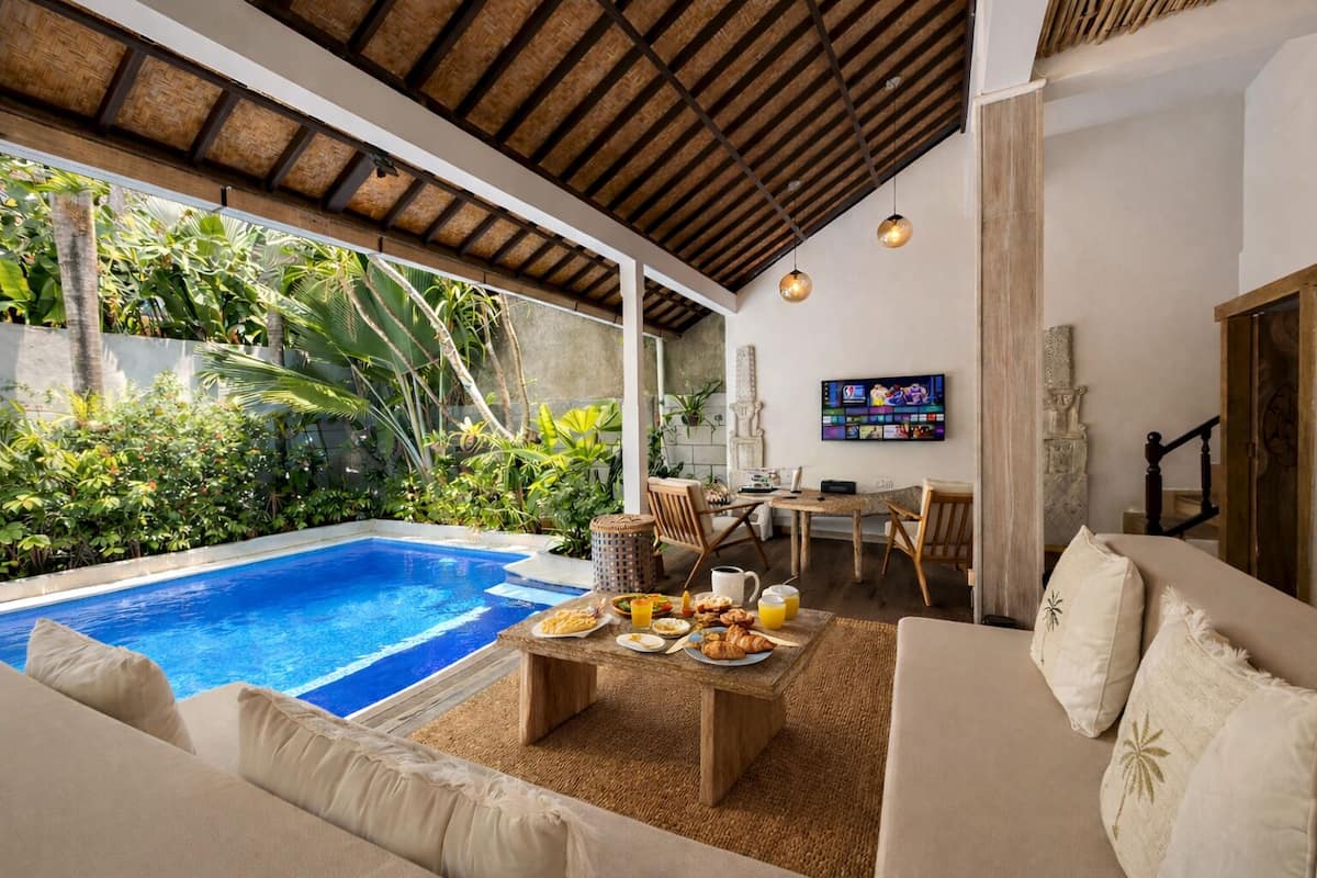 A poolside area with a dining table set for breakfast, a sofa, and a TV in the background.