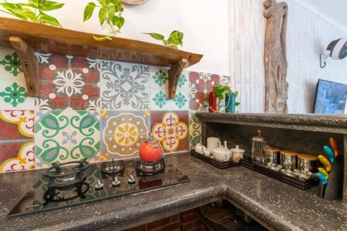 Uma cozinha com azulejos coloridos, um fogão a gás e uma prateleira com utensílios de cozinha.