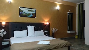 Una habitación de hotel con una cama grande, dos mesitas de noche, un aparador, un cuadro en la pared y una ventana con cortinas.