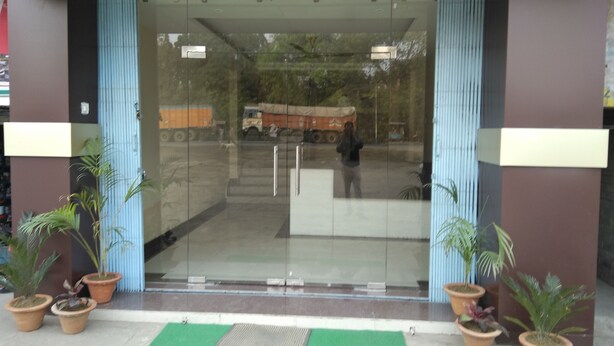 Entrada de un edificio con puertas de vidrio, plantas en macetas y un felpudo verde.