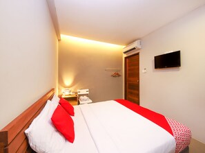 Habitació d'hotel amb llit, televisió, aire condicionat, taula de nit i televisió penjada a la paret.