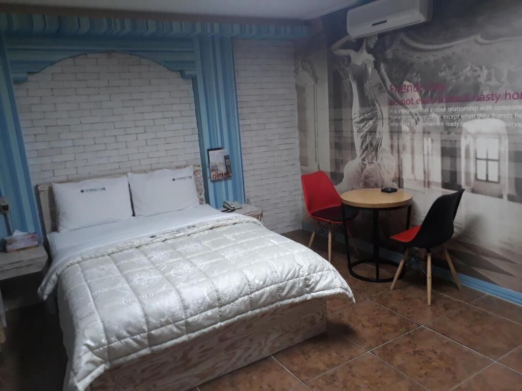 Un dormitorio con una cama, una mesita pequeña con dos sillas y un mural en la pared.